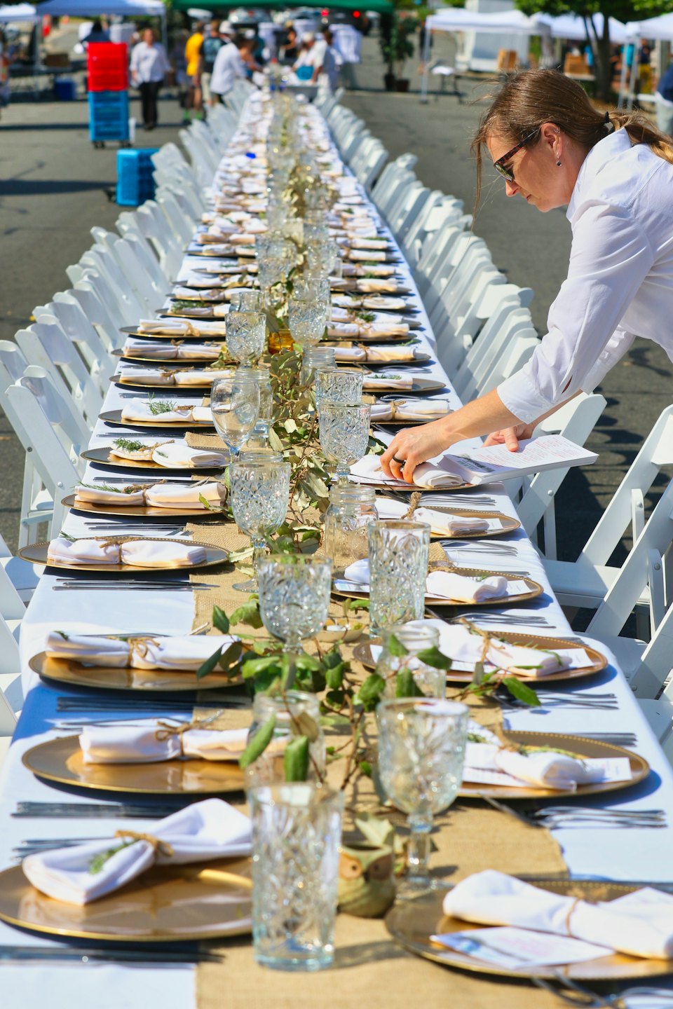 Event planner arranging place settings on a long outdoor dining table.