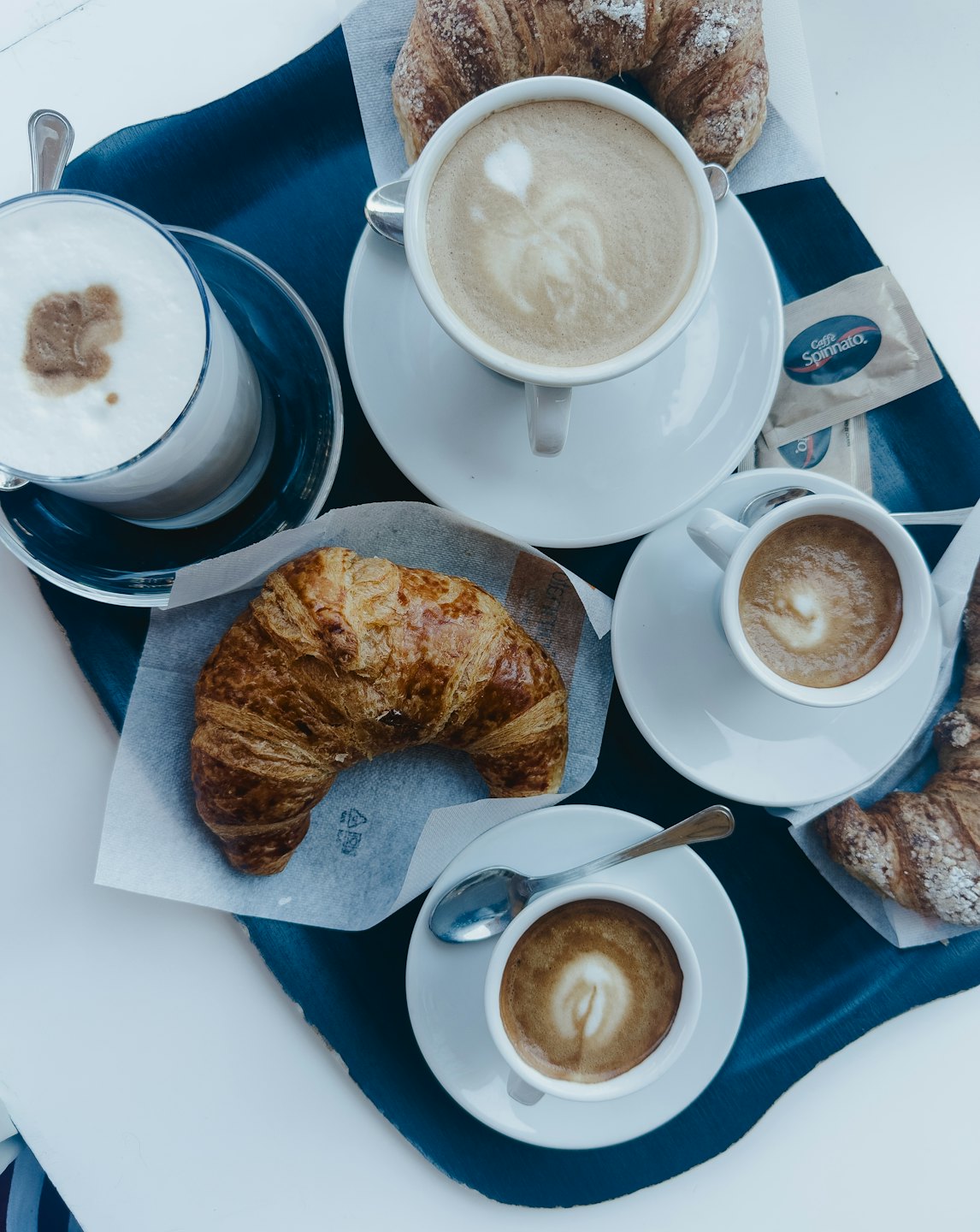 Four cups of coffee and three croissants on a tray.