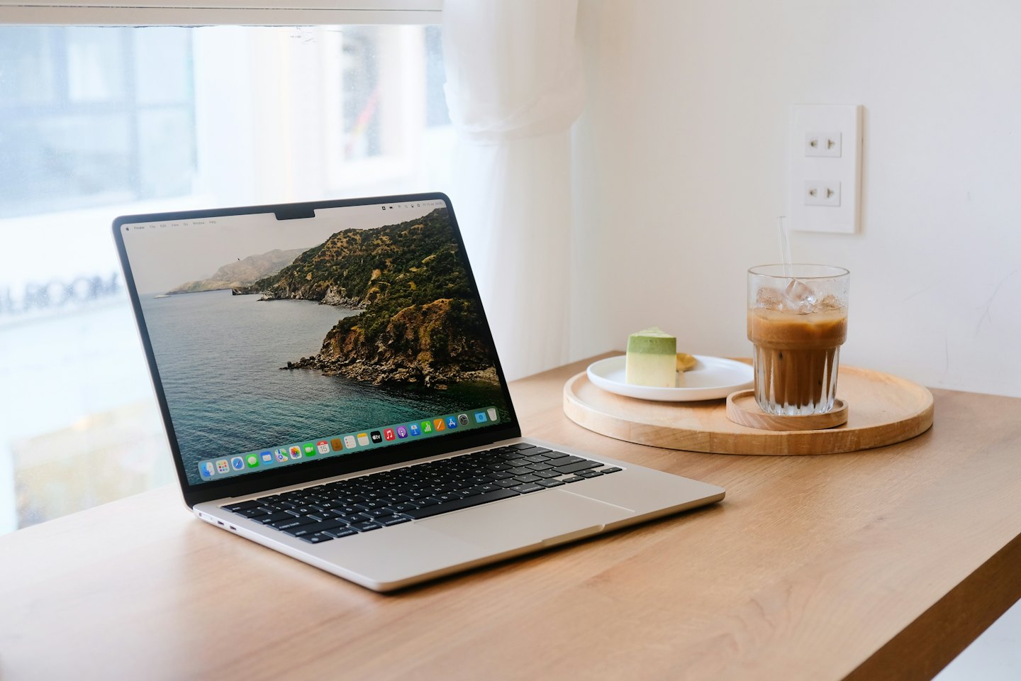 Laptop on wooden table with iced coffee and green cake.